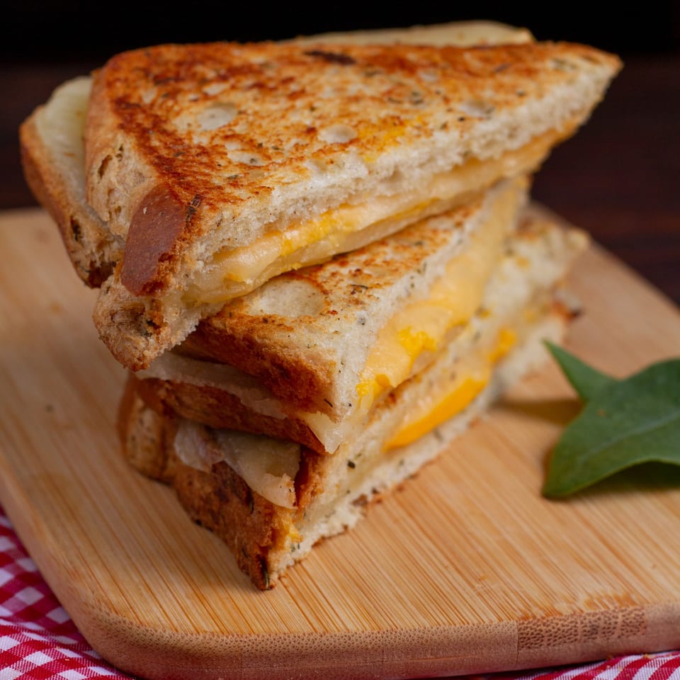 Stack of two golden-brown grilled cheese sandwiches with melted yellow cheese on a wooden board.